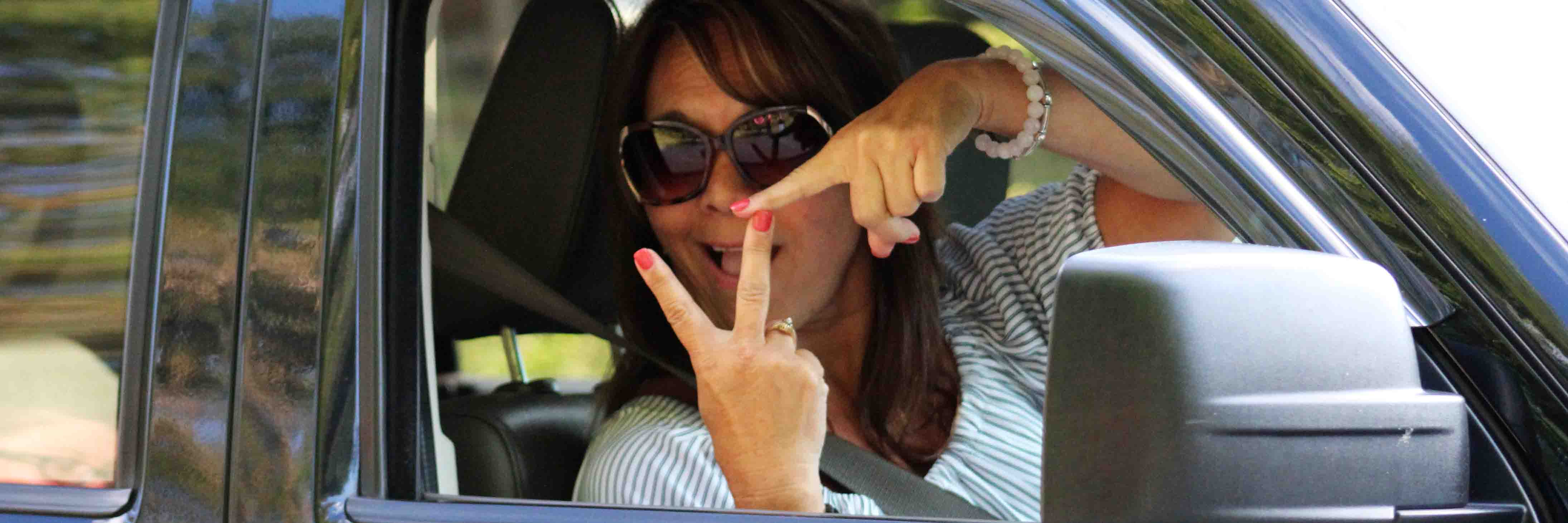 A woman in sunglasses showing the VT hand sign through a vehicle window