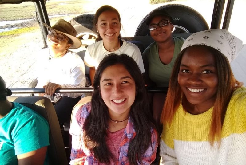 Five young women sit in the back two seats of a large, windowless vehicle