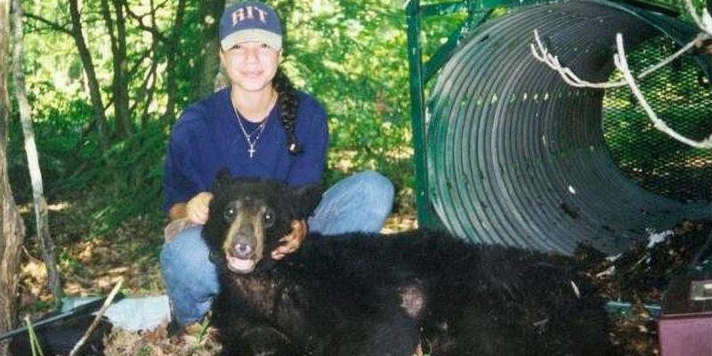 A female in a wooded area holds the head of a sedated bear