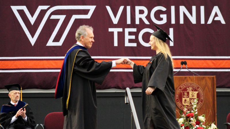 Dean Paul M. Winistorfer fist bumping a recent graduate on stage at commencement.