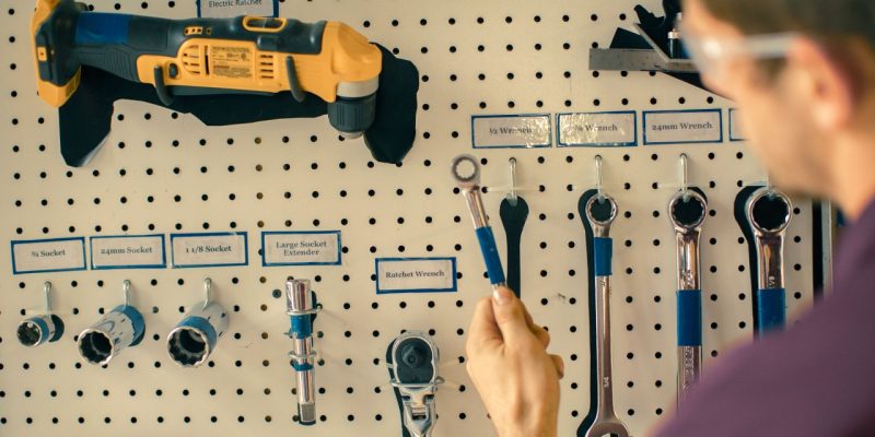 A student replacing a wrench on a pegboard labeled with tool names and marked with their corresponding silhouette.