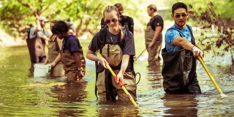 Students wearing waders holding poles and nets in a stream. 