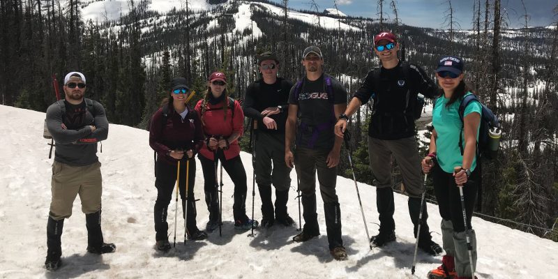 Seven students standing side by side on a snow-covered mountain peak.