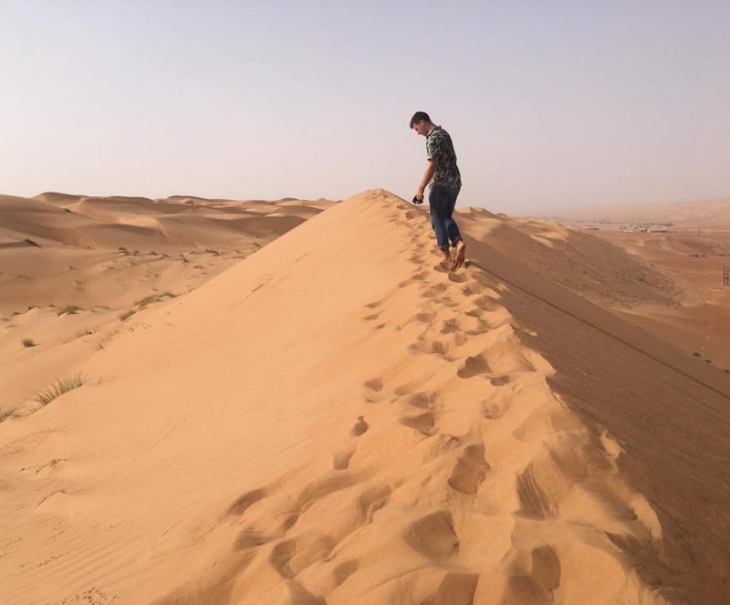 A young man walking along the top of a sand dune barefoot in Oman.