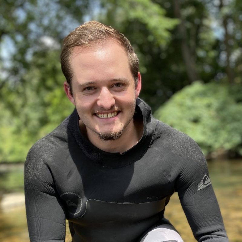 A person in a wetsuit stands in a stream.