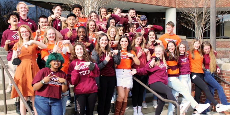 Students dressed in orange and maroon throw the Hokie "VT" hand sign.