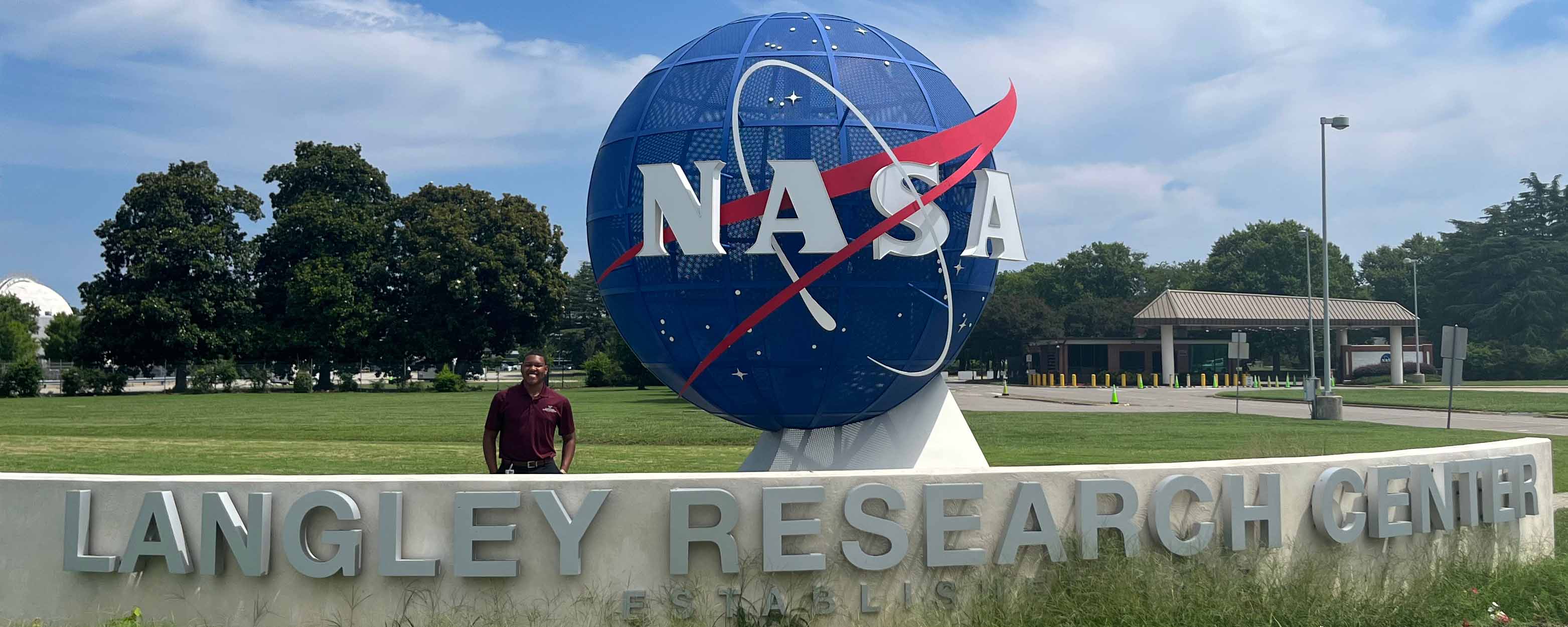 An intern standing under the NASA logo as a sphere at the entrance of Langley Research Center.