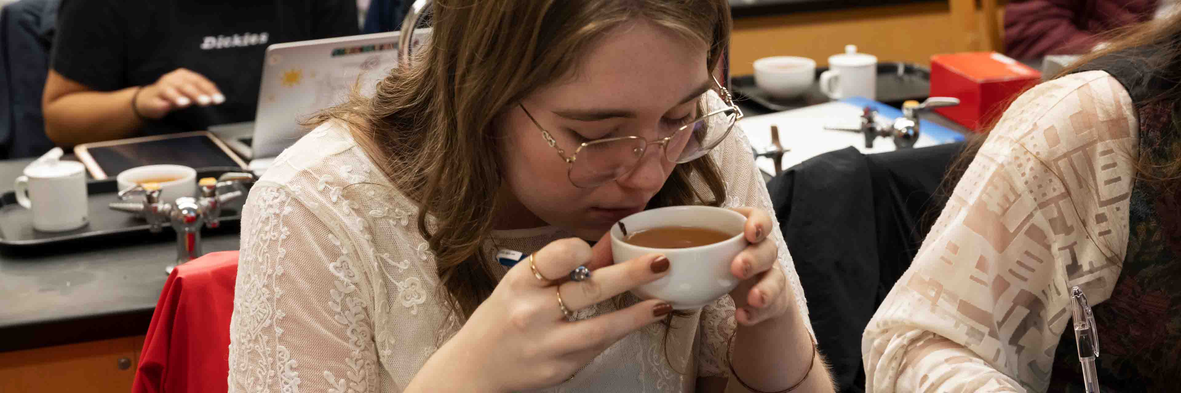 A student holding a cup of tea with both hands to her nose and mouth