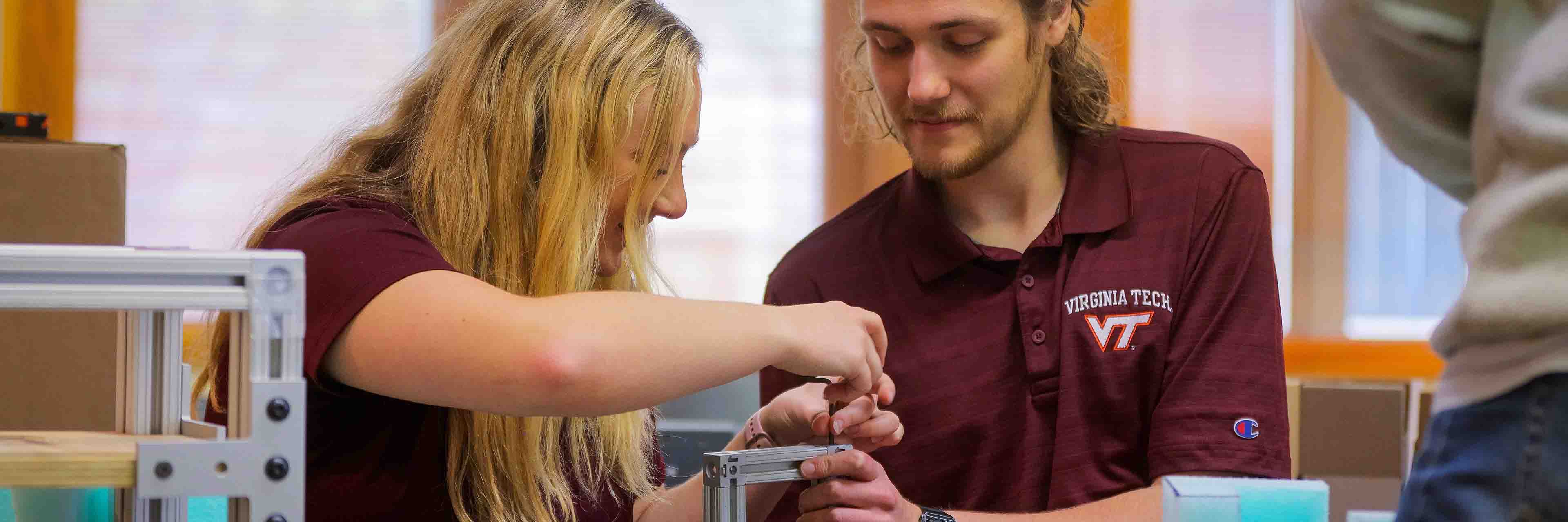 A student holds a metal frame while another turns a screw.