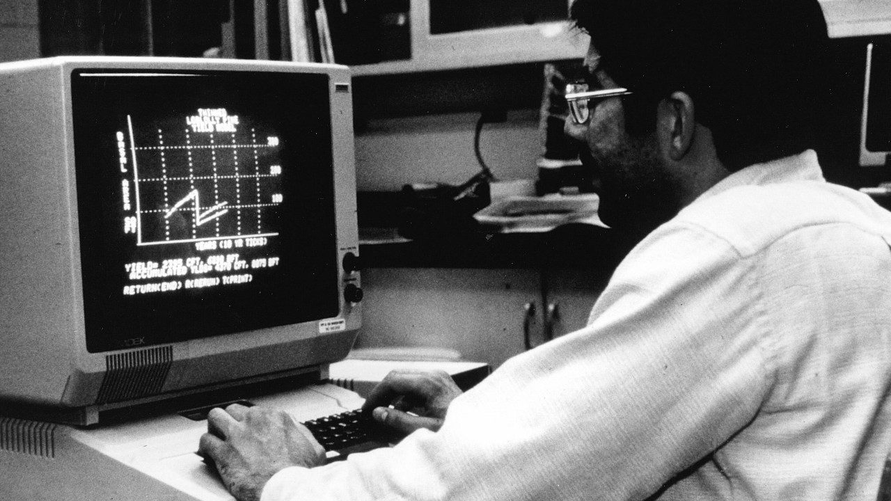 Man typing on a keyboard looking at a graph on an old computer screen
