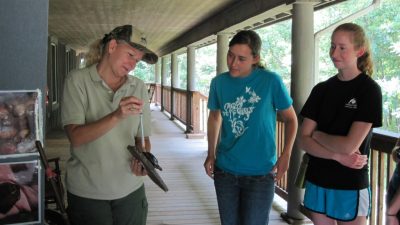 Amy Roberts (L) of the Virginia Department of Game and Inland Fisheries demonstrates to Heather Meslar (C) and Cari Lynn Squibb,  how to measure a turtle's weight using a pesola scale.
