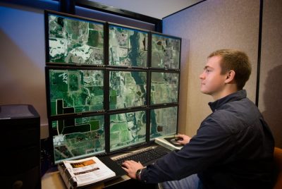 Researcher studying satellite images on nine monitors.