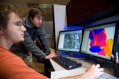 Two students looking at maps on monitors.