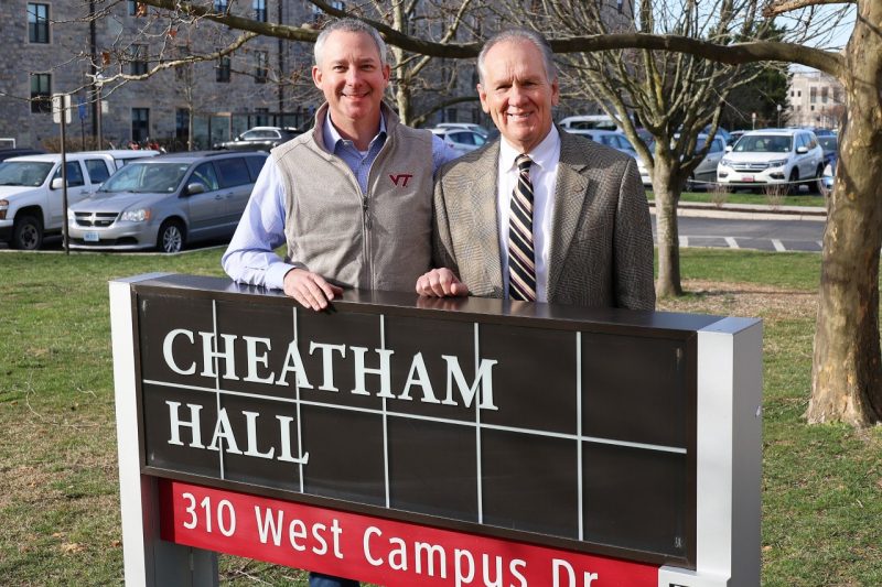 Two men stand behind a waist high location sign that reads Cheatham Hall , 310 West Campus Dr.