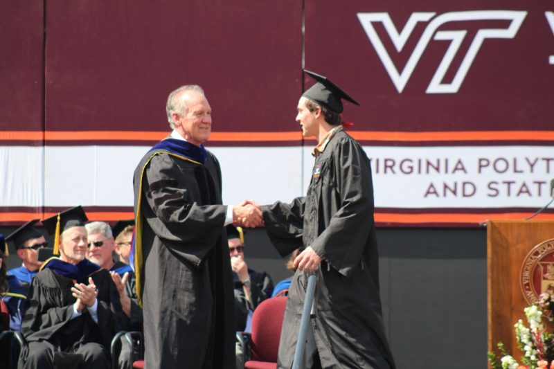 A graduating student in cap and gown shakes the dean's hand on stage at commencement