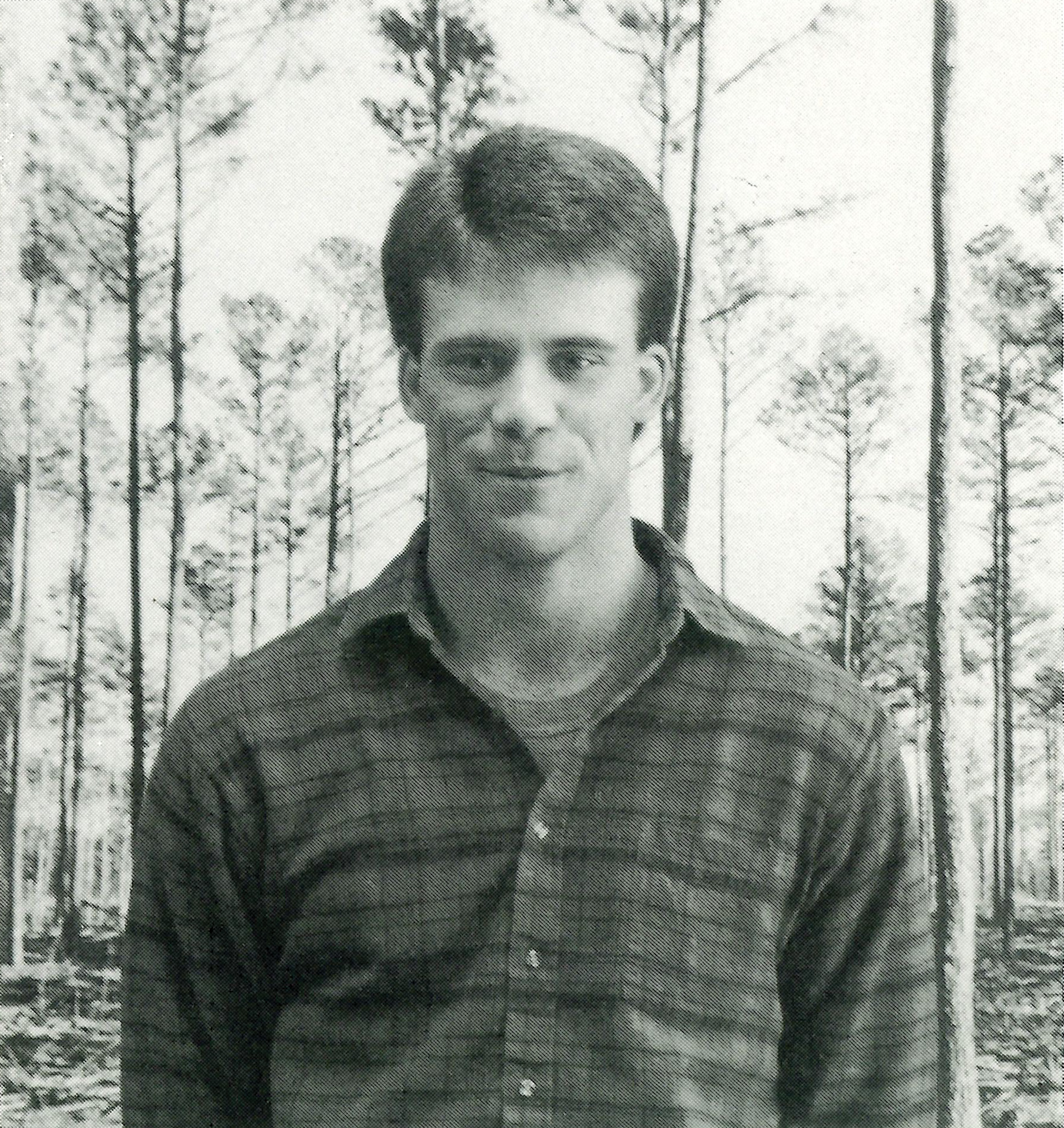 A black and white photo from 1989 of Easton Loving standing front of a backdrop of tall skinny pine trees.