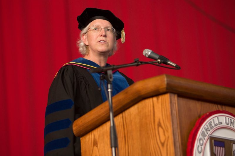 A woman wearing academic regalia standing at a podium that reads Cornell University.