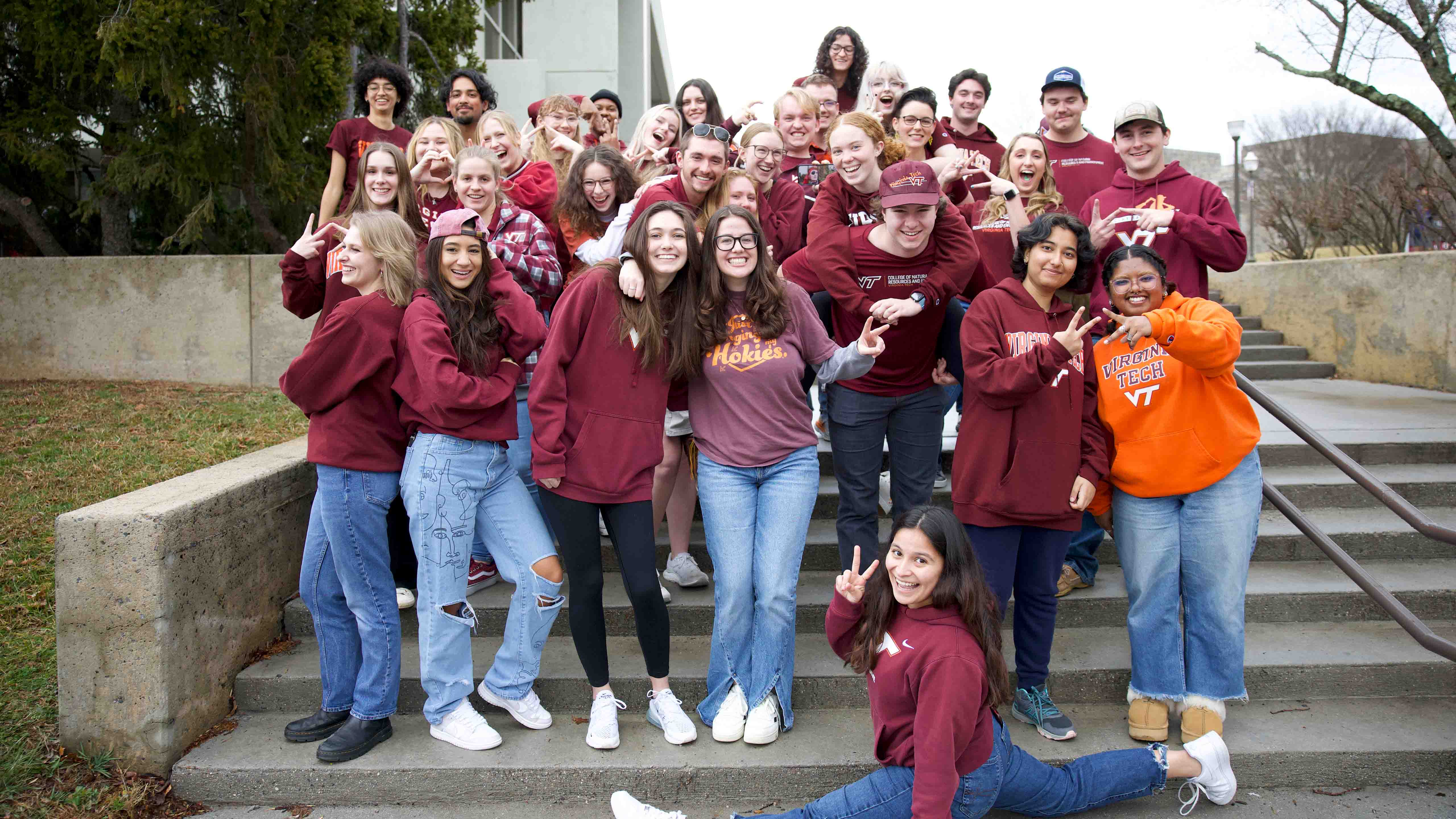 Student ambassadors posing outside on steps throwing the V T hand sign, one student doing the splits