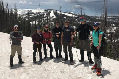 Seven students standing side by side on a snow-covered mountain peak.