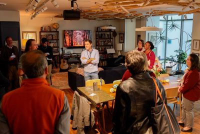 A group of people stand around a table in an apartment’s living room.