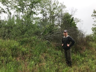 Man in jacket stands next to the invasive autumn olive, a green shrub