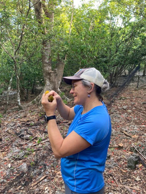 woman in blue shirt holds a piece of fruit in a forest