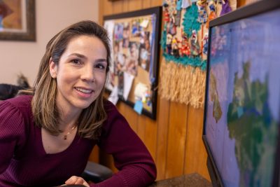 woman with brown hair in maroon sweater looks at maps on a screen and smiles