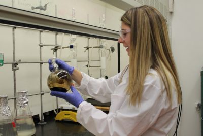 A student holds a glass beaker with dark material separating from clear liquid.