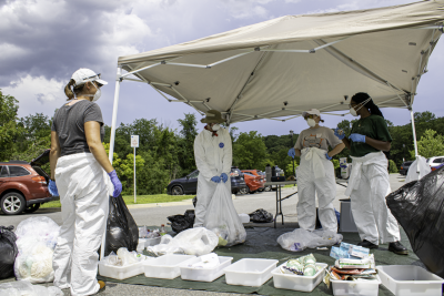 Jennifer Russell and three undergraduate students are wearing protective attire and sorting waste.